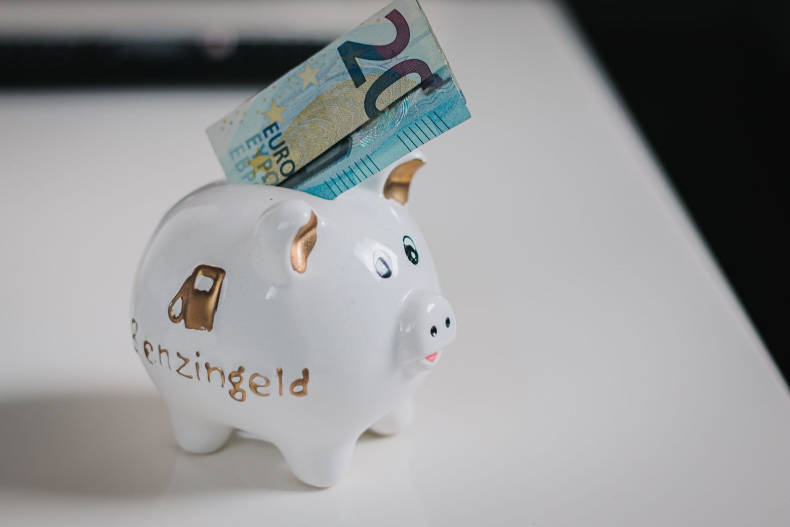 A white piggy bank with a €20 note inserted, symbolizing savings.